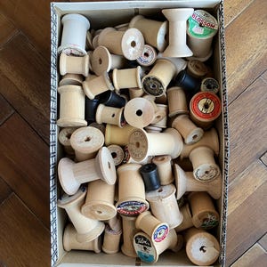 May include: A box filled with wooden spools of thread. The spools are various sizes and have different labels, including "Blossom" and "Talon's".