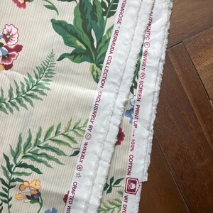 May include: Cream fabric with a floral design of red, blue, and yellow flowers, and green leaves. The fabric has vertical stripes and the text "PRIMROSE BERMUDA COLLECTION" and "100% COTTON".