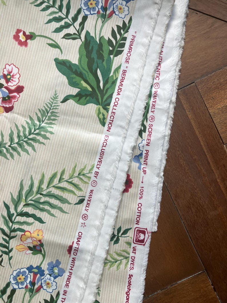 May include: Cream fabric with a floral design of red, blue, and yellow flowers, and green leaves. The fabric has vertical stripes and the text "PRIMROSE BERMUDA COLLECTION" and "100% COTTON".