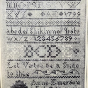 May include: A framed cross-stitch sampler with black thread on a light background. The sampler includes the alphabet, numbers, and the text "Let Virtue be a Guide to thee." It is signed "Anne Emerson aged 7 years."