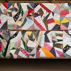 May include: A collection of eight patchwork quilt blocks, each featuring a unique arrangement of fabric scraps. The blocks showcase a variety of colors and patterns, including stripes, florals, and geometric shapes. The blocks are displayed in a wooden frame.