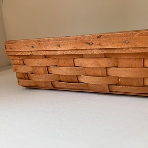 May include: A rectangular woven basket made of light brown wood strips. The basket features a horizontal rim secured with small metal nails along the top edge. The sides are constructed with a classic over-under weave pattern using flat wooden splints.