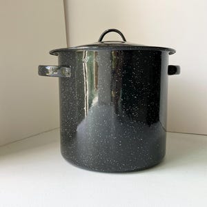 May include: A large, black speckled enamel pot with a matching lid. The pot has two side handles and a loop handle on the lid. This cooking pot is suitable for soups, stews, and canning.