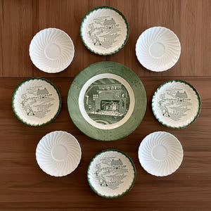 May include: A collection of vintage dinnerware featuring a large green and white plate with a detailed interior scene, surrounded by smaller plates with a green border and a pastoral design, and white saucers with a spiral pattern.
