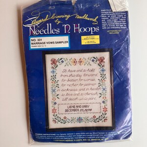 May include: A Needles 'N Hoops marriage vows sampler embroidery kit in a plastic package. The blue packaging features the text No. 331 Marriage Vows Sampler, framed size 12 x 14 inches, and displays a floral-bordered sampler with the text Liene and Gary December 23, 1978.