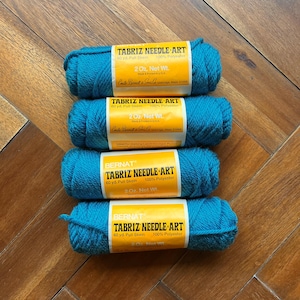 May include: Four spools of turquoise blue yarn labeled "Bernat Tabriz Needle Art" with a yellow label. Each spool is 60 yards and 2 ounces of 100% polyester.