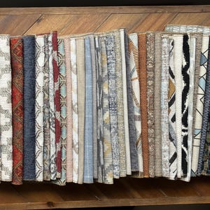 May include: A collection of fabric swatches in various colors and patterns, including paisley, geometric, and striped designs. The swatches are arranged in rows on a wooden surface.