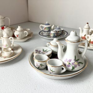 May include: A white ceramic mug with a black handle and the text "But First, Coffee" in a handwritten style. The mug is on a white surface. The mug is approximately 4 inches tall.