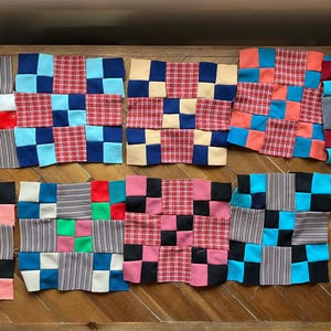 May include: A collection of colorful fabric squares arranged on a wooden surface. The squares feature various patterns and colors, including red, blue, black, and pink, creating a patchwork design. The squares are arranged in rows.
