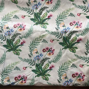 May include: Cream-coloured fabric with a floral pattern. The design includes bouquets of pink, blue, and yellow flowers, interspersed with green fern leaves, set against a backdrop of vertical stripes. The fabric has a sheen.