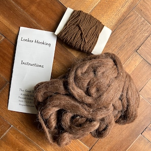 May include: A collection of brown fiber and yarn for locker hooking. The image includes a bundle of loose, fluffy fiber, a small spool of tightly wound yarn, and a white paper with "Locker Hooking Instructions" printed on it.