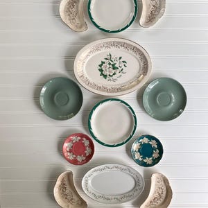 May include: A collection of ceramic tableware including two round plates with green rims, two oval platters with floral patterns, four crescent-shaped dishes with brown botanical designs, two solid sage green saucers, and two small floral saucers.