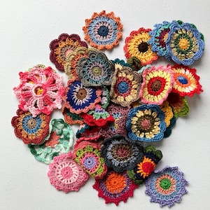 May include: A collection of colorful, handmade crochet flowers in various shapes and sizes. The flowers feature a variety of colors, including pink, blue, yellow, and green. Some are round, while others are square or have scalloped edges. These crochet flowers are perfect for crafting projects.