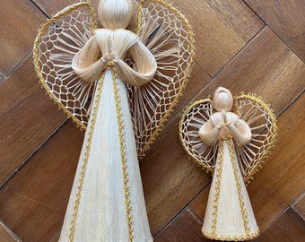 May include: Two straw angel figurines. The angels have cream-coloured cone-shaped dresses, straw hair, and delicate wings with gold trim. The wings are heart-shaped. The larger angel is approximately 20 cm tall, and the smaller angel is about 13 cm tall.