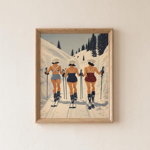Könnte beinhalten: Ein gerahmter Kunstdruck zeigt drei Figuren von hinten, die weiße Pelzmützen, Badeanzüge in Hellblau, Dunkelblau und Kastanienbraun sowie Skischuhe tragen und Skistöcke halten. Sie stehen auf einem verschneiten Pfad zwischen Tannenbäumen.
