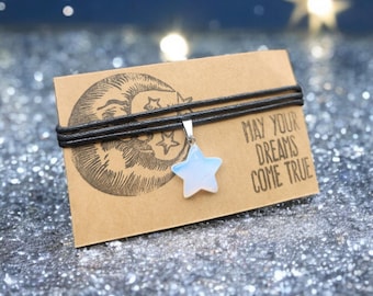 May include: A black leather cord necklace with a white opal star charm. The necklace is displayed on a brown card with the text "May your dreams come true".