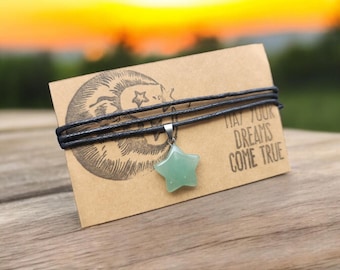 May include: A black cord necklace with a green star-shaped pendant. The necklace is on a brown card with the text "May your dreams come true".