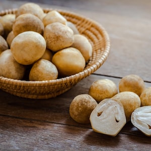 May include: A wicker basket overflowing with round, light brown mushrooms, with some scattered on a wooden surface. One mushroom is cut open, showing a white interior. The mushrooms are a light tan colour.