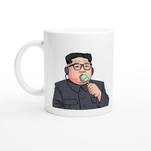 以下が含まれることがあります： 緑色のアイスキャンディーを食べる、眼鏡と黒のスーツを着た男性の漫画の画像が描かれた白いセラミック製のマグカップです。