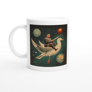 以下が含まれることがあります： 宇宙を飛ぶカモメに乗った男性のカラフルな画像が描かれた白いセラミックマグカップ。男性は銃を持っており、背景には惑星があります。