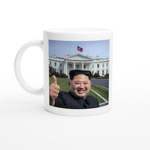 以下が含まれることがあります： 白いセラミック製のマグカップに、ホワイトハウスの前で男性が写っている写真がプリントされています。男性は親指を立てて笑顔を見せています。背景には、旗が掲げられたホワイトハウスがあります。