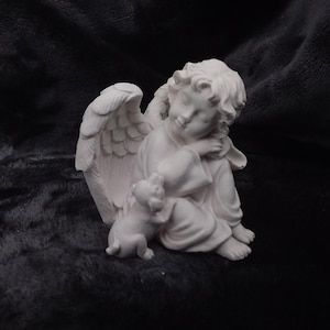 Puede incluir: Figura blanca de un ángel durmiente con alas detalladas, abrazando a un perro pequeño. El ángel está sentado, con la cabeza apoyada en el brazo. El perro está al lado del ángel. Fondo oscuro y texturizado.