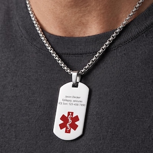 May include: A silver-toned metal dog tag pendant on a matching box chain necklace. The pendant features a red medical alert symbol and engraved text reading: Jason Decker, Epilepsy, seizures, ICE Son: 123-456-7890. The necklace rests against a dark gray shirt.