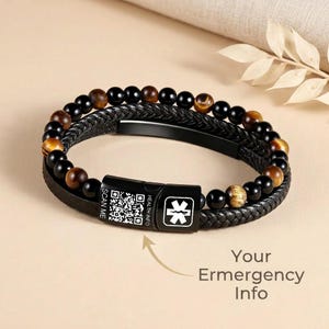 May include: A black leather bracelet with a braided design, featuring black and brown beads. The bracelet includes a clasp with a QR code and the text "HEALTH INFO". The text "Your Emergency Info" is also visible.