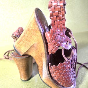 May include: A brown leather sandal with a woven design and a wooden heel. The sandal features a high heel and a woven strap that wraps around the ankle. The shoe has a classic, vintage look.