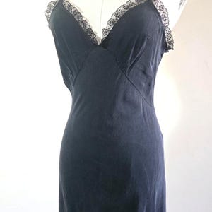 May include: A black slip dress with spaghetti straps and a V-neckline. The neckline and straps are trimmed with black lace. The dress is displayed on a mannequin.