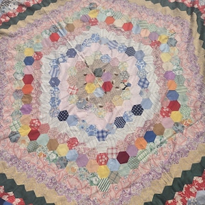 May include: A large handmade quilt featuring a hexagonal patchwork design. The quilt is composed of numerous small fabric hexagons in various colors, including red, blue, yellow, green, and pink, arranged in concentric rings around a center.