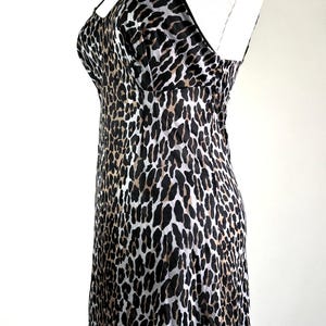 May include: A leopard print slip dress with thin straps. The dress features a bustier-style top and a flowing skirt. The animal print includes black, brown, and gray spots on a light background. The dress is displayed on a mannequin.