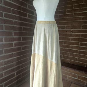 May include: A long, flowing skirt in a two-tone design. The top section is a light cream colour, transitioning to a soft yellow at the bottom. The skirt is displayed on a mannequin, showcasing its shape and drape.
