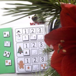 May include: A Christmas-themed educational activity set featuring a snowman, Christmas tree, and gingerbread man. The set includes number matching cards and a green background with additional matching cards.