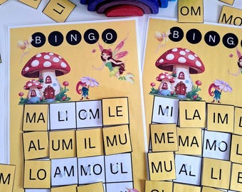 Könnte beinhalten: Zwei gelbe Bingo-Karten mit Pilz- und Feenillustrationen. Das Wort "BINGO" steht oben. Kleine gelbe Kacheln mit Buchstaben sind um die Karten herum verstreut. Oben befindet sich ein Holz-Regenbogen-Stapler.