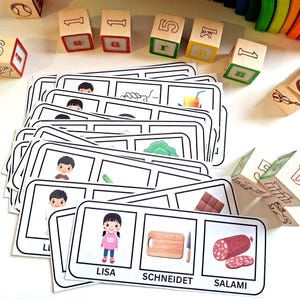 Puede incluir: Juego educativo con bloques de números de madera y tarjetas ilustradas. Las tarjetas muestran imágenes de personas, objetos y alimentos. Las palabras "LISA", "SCHNEIDET" y "SALAMI" están impresas en las tarjetas.