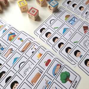 Puede incluir: Un conjunto de tarjetas did&aacute;cticas y bloques de madera. Las tarjetas did&aacute;cticas presentan ilustraciones de varios objetos y personas, mientras que los bloques de madera tienen letras y s&iacute;mbolos. Las tarjetas y los bloques est&aacute;n dispuestos sobre una superficie blanca.