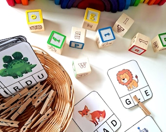Könnte beinhalten: Eine Sammlung von Lernspielzeugen, darunter Holzbuchstabenblöcke, Tierkarten und ein Regenbogen-Holzbogen. Die Blöcke zeigen Buchstaben und Zahlen, die Karten Tierillustrationen. Ein Weidenkorb enthält Wäscheklammern.