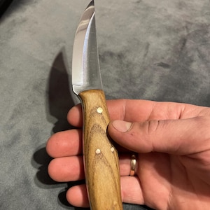 May include: A small, curved knife with a wooden handle. The handle has brass accents and a hole at the bottom.