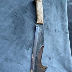 May include: A large, curved, stainless steel knife with a wooden handle. The handle has three brass rivets. The knife is lying on a blue fabric surface.