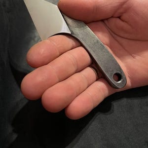 Op de afbeelding: Een klein, zilveren mes met een afgeronde handgreep. Het mes heeft een gat in de handgreep voor een koord.