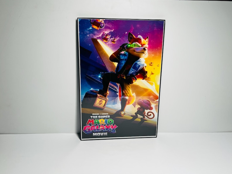 May include: A framed movie poster featuring a fox-like character in a blue and white outfit, holding a laser gun. The poster has a vibrant, colorful background with the text "THE SUPER MARIO GALAXY MOVIE" at the bottom.