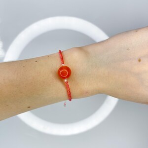 Op de afbeelding: Een rood en wit kralenarmband met een enkele oranje edelsteenkralen.
