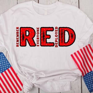 May include: White t-shirt with the word "RED" in large red letters. The letters are filled with a red, white, and blue pattern. The words "Remember Everyone Deployed" are written in black letters above and below the word "RED".