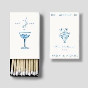 Könnte beinhalten: Eine weiße Streichholzschachtel mit einer blauen Illustration eines Martini-Glases mit Eis und dem Wort "gin" zweimal geschrieben. Die Streichholzschachtel hat auf der Rückseite ein blaues und weißes Blumenmuster mit dem Text "THE WEDDING OF AMBER & MICHAEL New Orleans 6.11.25"