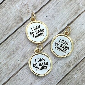 May include: Three gold-coloured charms with a white background and black text that reads "I can do hard things".