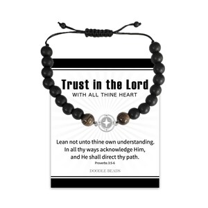 May include: Black beaded bracelet with a compass charm and the text "Trust in the Lord, With All Thine Heart". The bracelet also includes the text "Lean not unto thine own understanding. In all thy ways acknowledge Him, and He shall direct thy path. Proverbs 3:5-6 Doodle Beads".