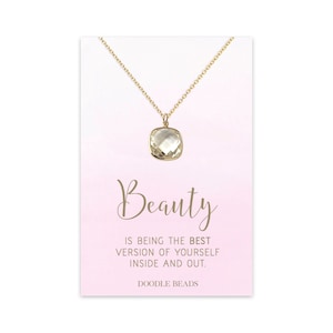 Könnte beinhalten: Eine goldfarbene Halskette mit einem quadratischen, hellgrünen Edelsteinanhänger. Die Halskette wird auf einer rosa-weißen Karte mit dem Wort "Beauty" und dem Satz "is being the best version of yourself inside and out." präsentiert.