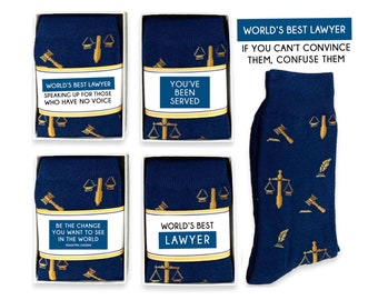 Könnte beinhalten: Vier Geschenkboxen mit blauen und goldenen Socken. Jede Box hat einen anderen Spruch auf der Vorderseite. Die Socken haben ein Muster aus Justizwagen, Hammer und Federkiel. Der Text auf den Boxen lautet: "World's Best Lawyer Speaking Up For Those Who Have No Voice", "You've Been Served", "Be The Change You Want To See In The World Mahatma Gandhi", und "World's Best Lawyer".
