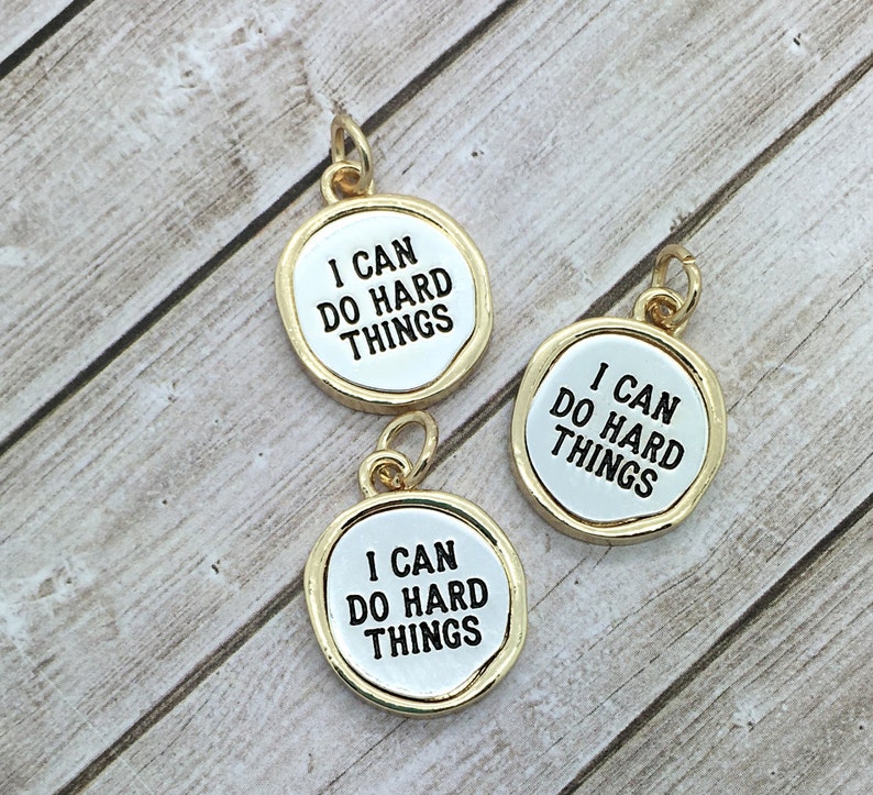 May include: Three gold-coloured charms with a white background and black text that reads "I can do hard things".